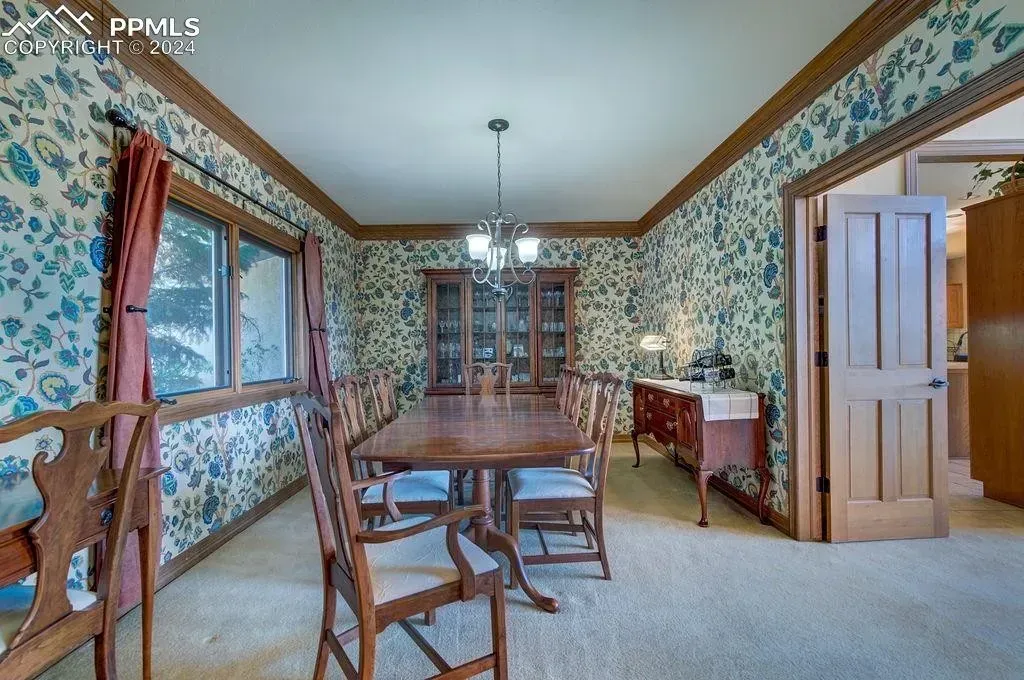 A dining room with a wooden table and chairs and floral wallpaper.