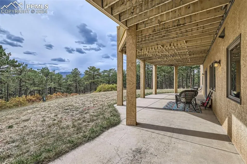 A large covered patio with a wooden deck and trees in the background.