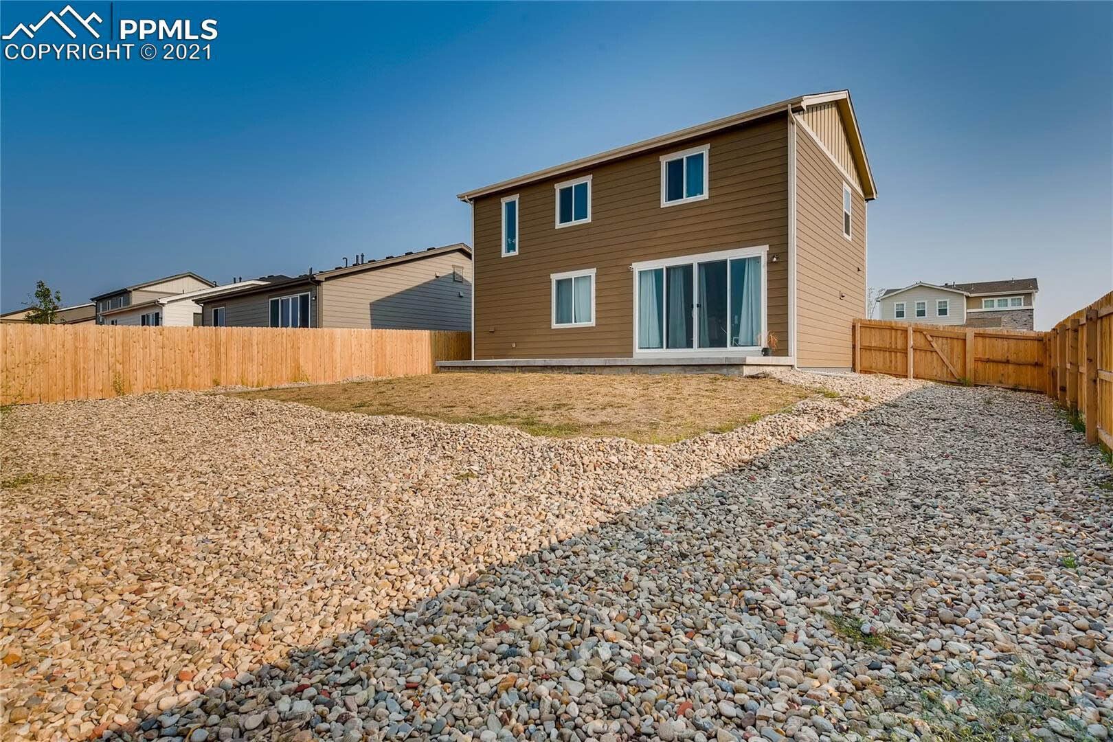 The backyard of a house with a gravel driveway and a wooden fence.