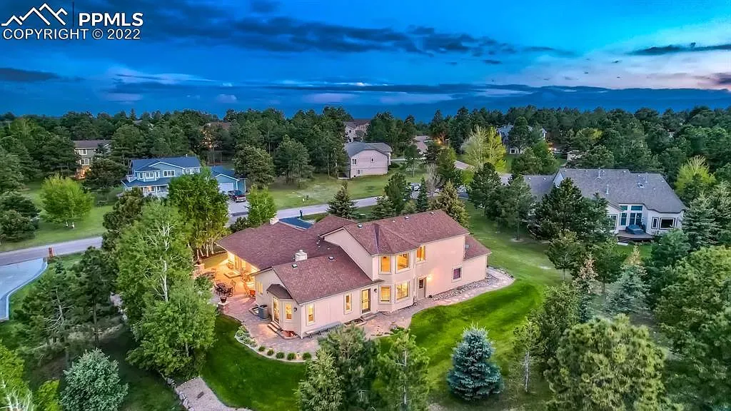 An aerial view of a large house surrounded by trees in a residential area.