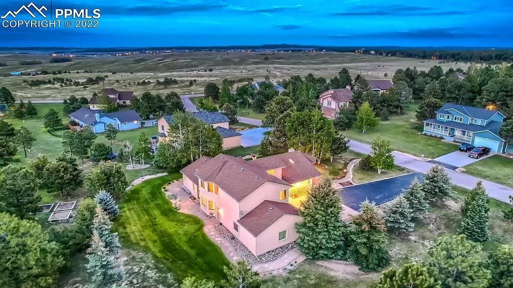 An aerial view of a large house in a residential area surrounded by trees.