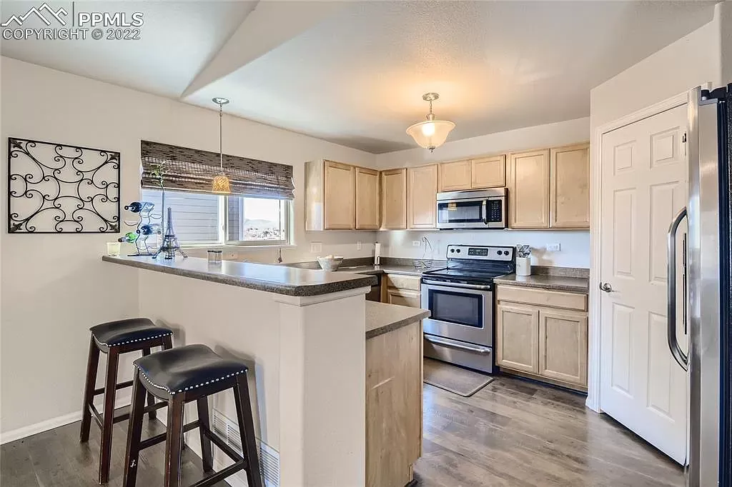 A kitchen with stools , a refrigerator , a stove , and a sink.