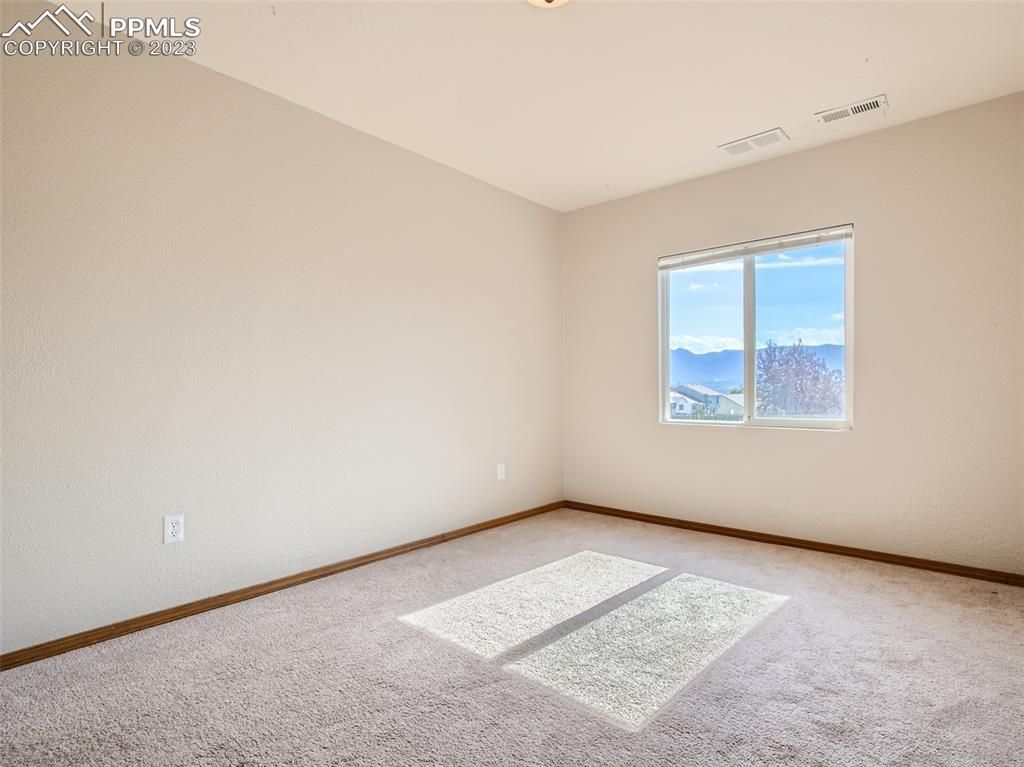 An empty bedroom with a large window and a carpeted floor.