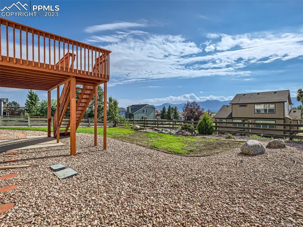 A wooden deck with stairs leading up to it is in the backyard of a house.