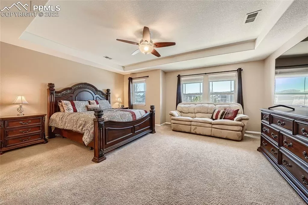 A bedroom with a bed , couch , dresser , nightstand and ceiling fan.