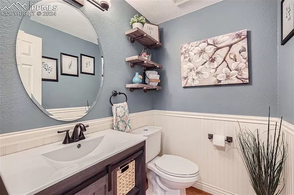 A bathroom with a sink , toilet , mirror and shelves.