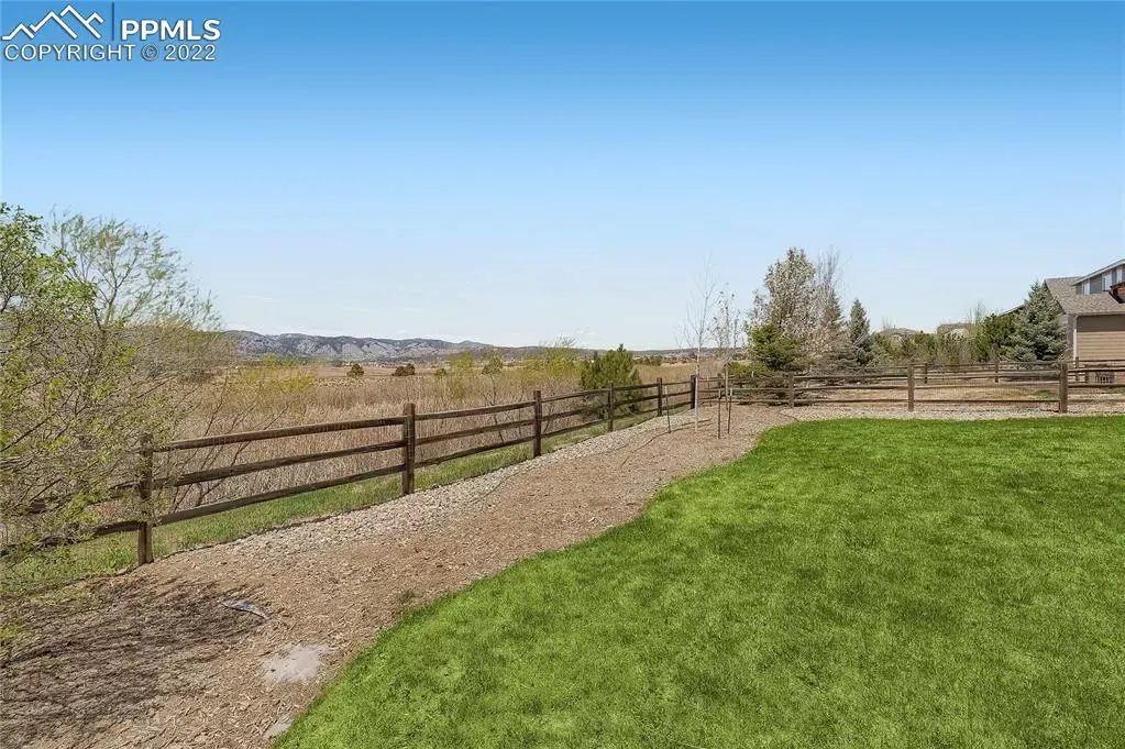 A wooden fence surrounds a large lush green field.
