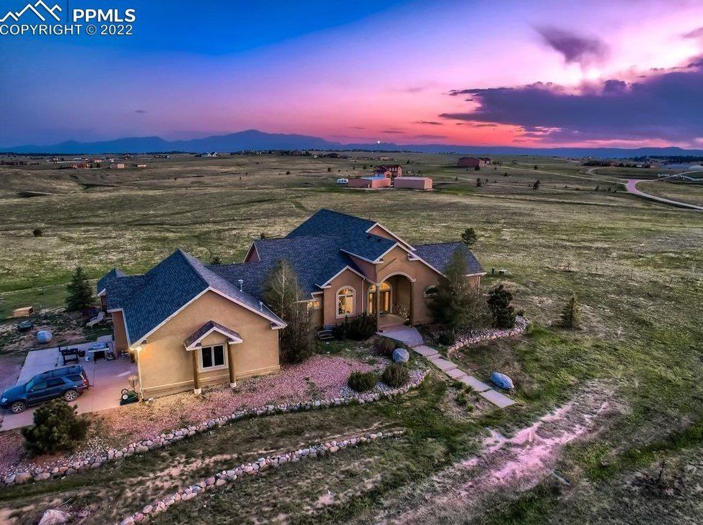 An aerial view of a house in the middle of a field at sunset.