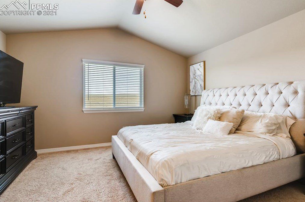 A bedroom with a large bed , dresser , television and ceiling fan.