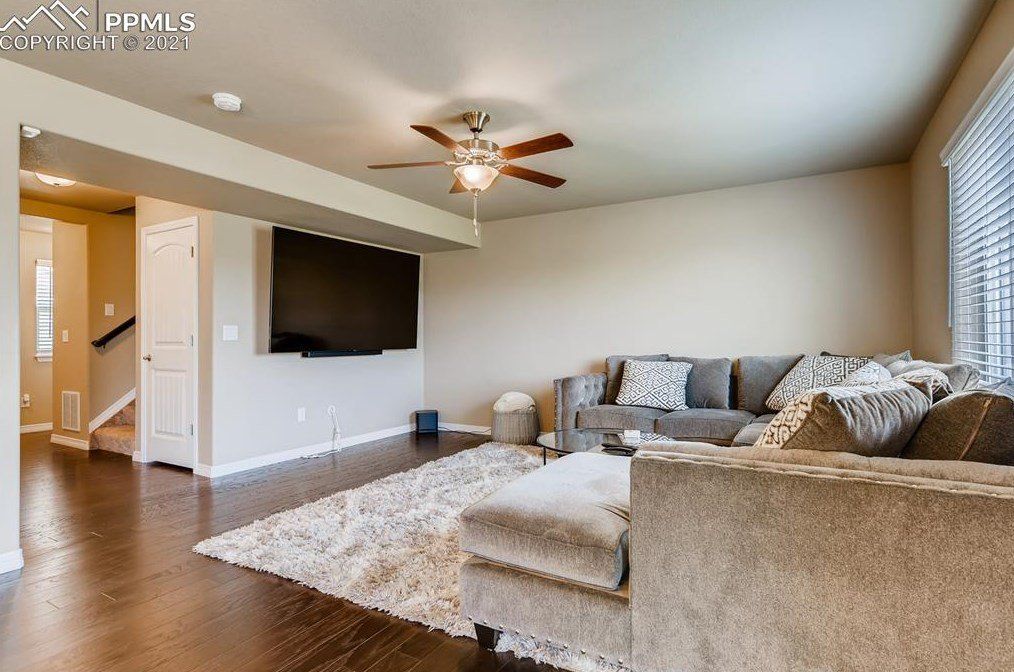 A living room with a couch , chair , television and ceiling fan.