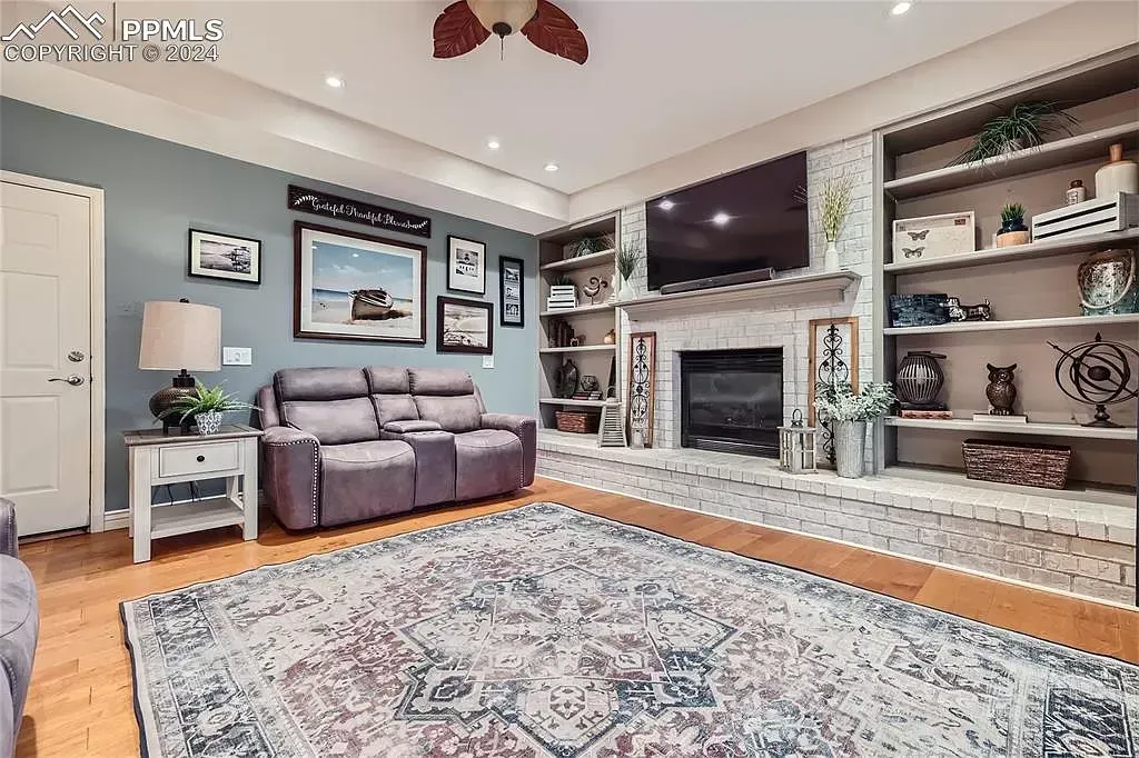 A living room with a couch , fireplace , rug and ceiling fan.