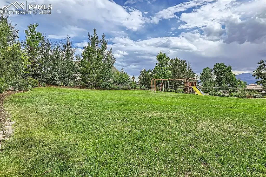 A large lush green field with a playground in the background.
