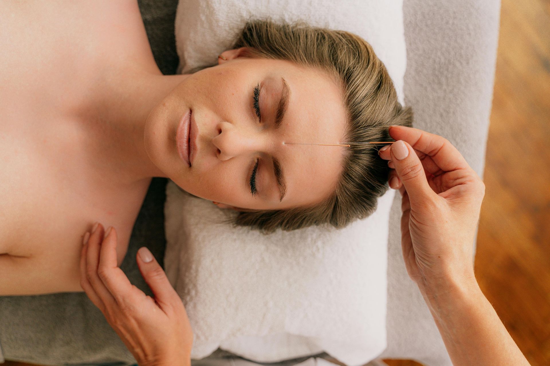 Mujer recibiendo un relajante masaje facial mientras está tumbada sobre una toalla blanca.