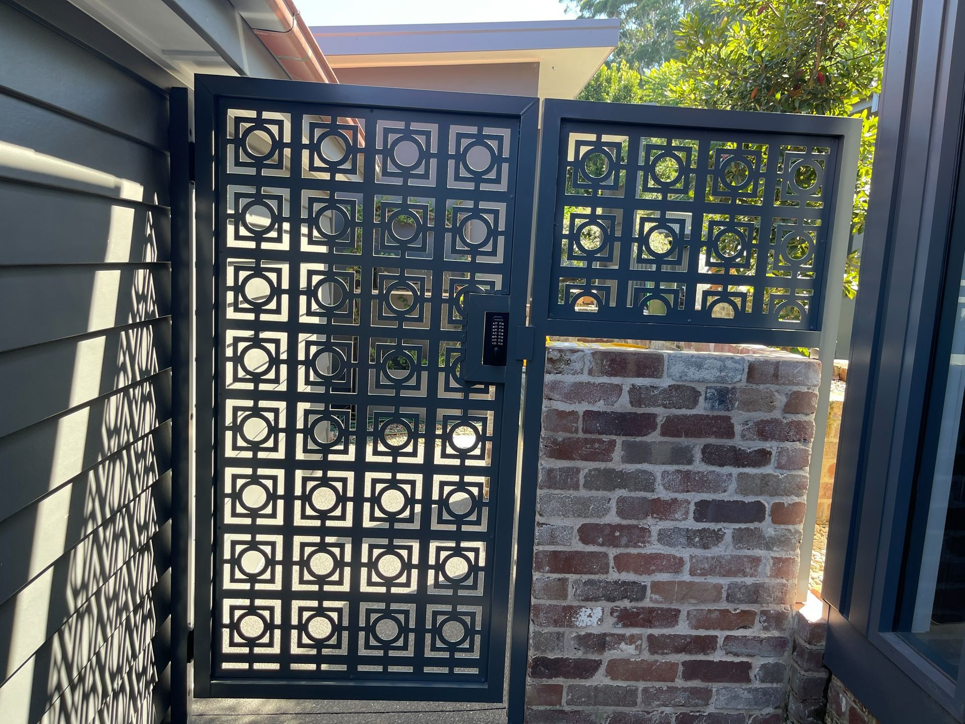 A black gate is sitting next to a brick wall.