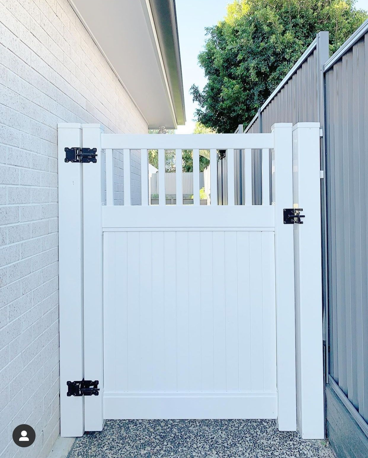 White wooden side gate with vertical slats beside a house and gray fence in a narrow outdoor passage