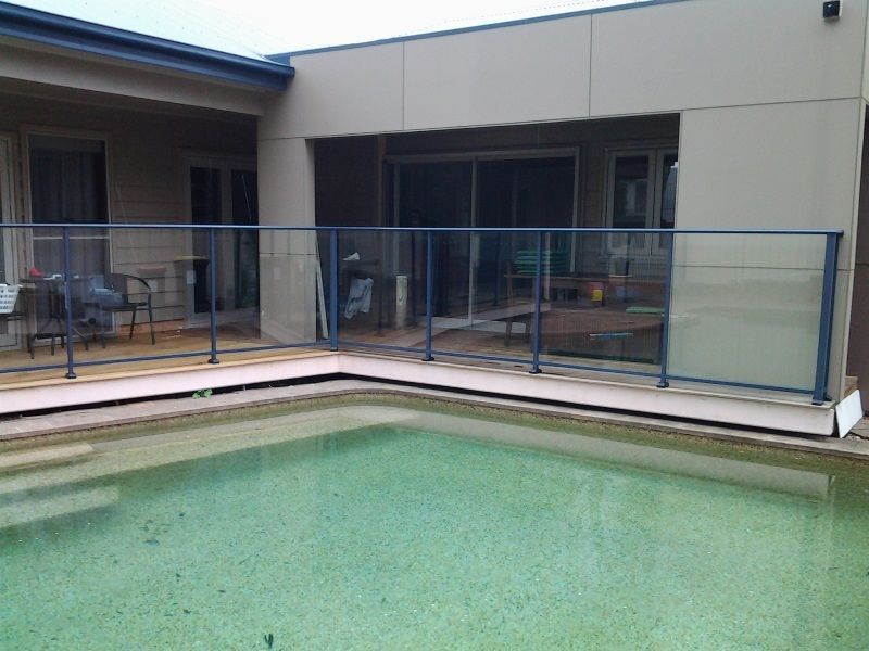 A swimming pool with a glass railing in front of a house.
