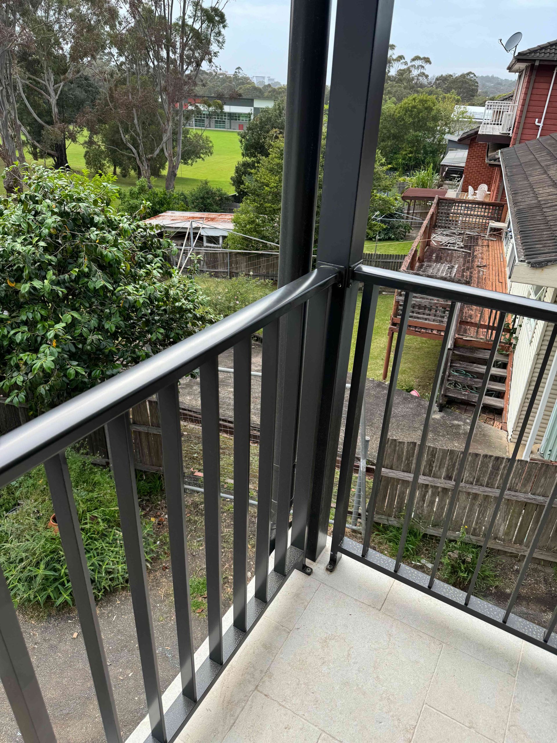 A balcony with a metal railing overlooking a lush green field.