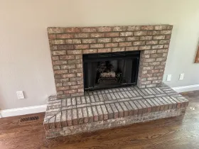 Brick fireplace with black insert and raised hearth in a carpeted living room.