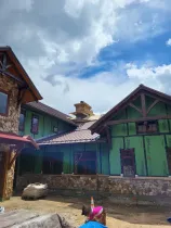 Colorful rustic cabins with stone walls under a cloudy blue sky, with a person in a pink hat at the bottom.