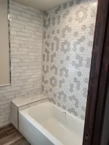 Small bathroom with white brick walls, patterned wallpaper, and a white bathtub next to a window.