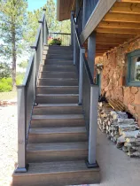 Outdoor wooden staircase with black railings beside a stone-and-wood building
