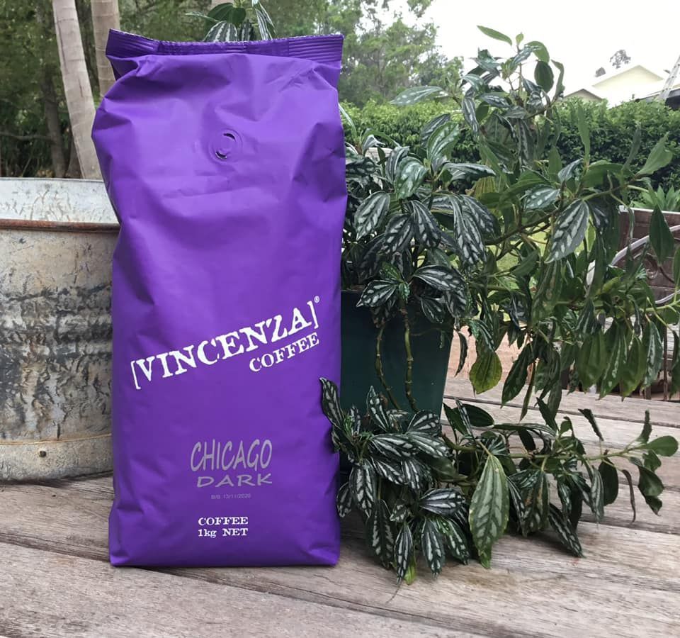 A Purple Bag of Coffee is Sitting on a Wooden Table Next to a Plant — Labroco Gourmet Coffee Supplier In Forster, NSW