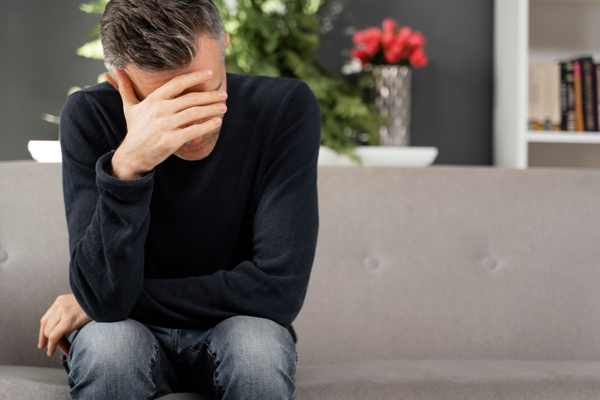 Man sitting on a sofa with his head in his hand, looking distressed.