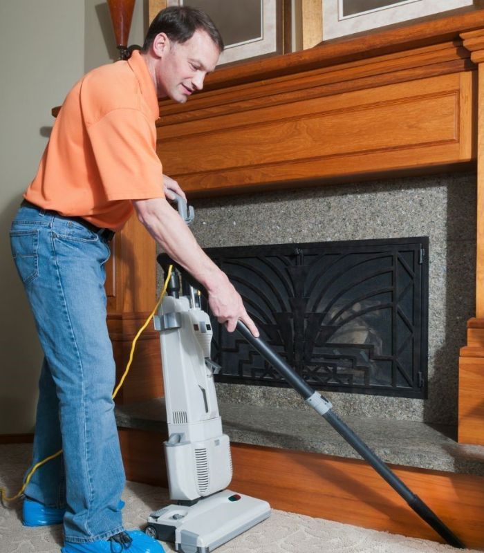A man is using a vacuum cleaner in front of a fireplace