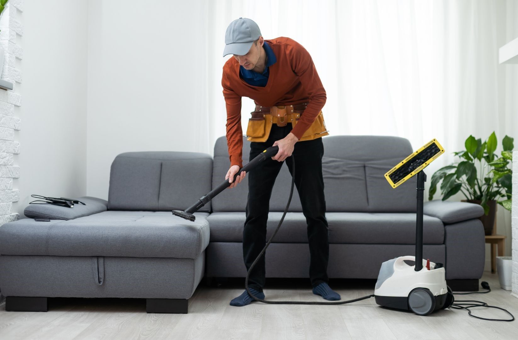 A man is cleaning a couch with a vacuum cleaner in a living room.