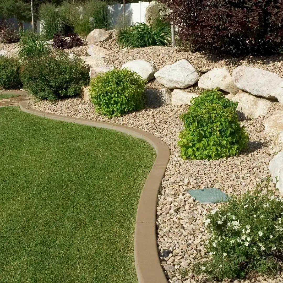 Curved lawn edge with tan gravel, green shrubs, and large rocks in a landscaped garden