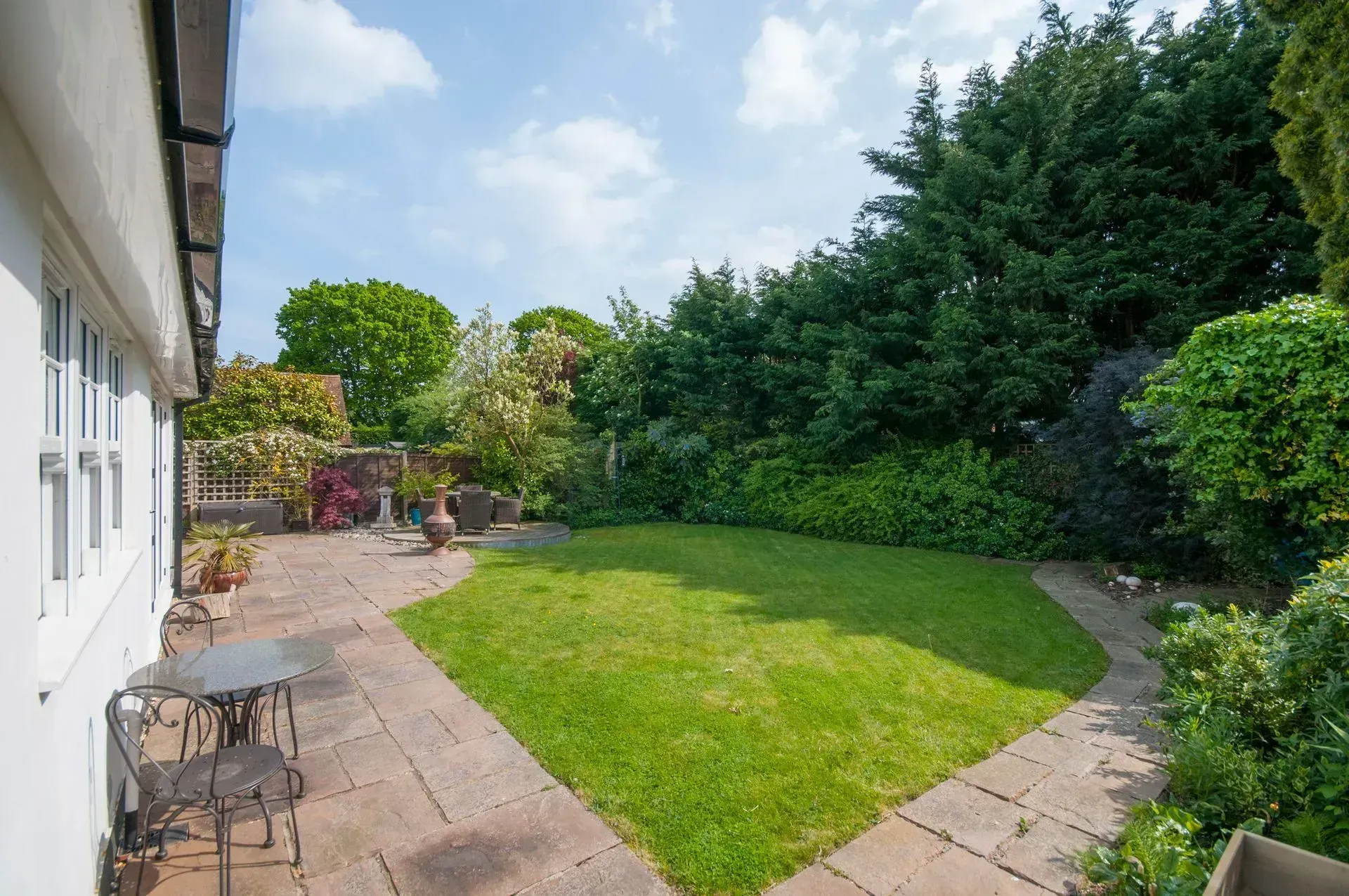 Backyard patio with grass lawn, surrounded by greenery and a white house.