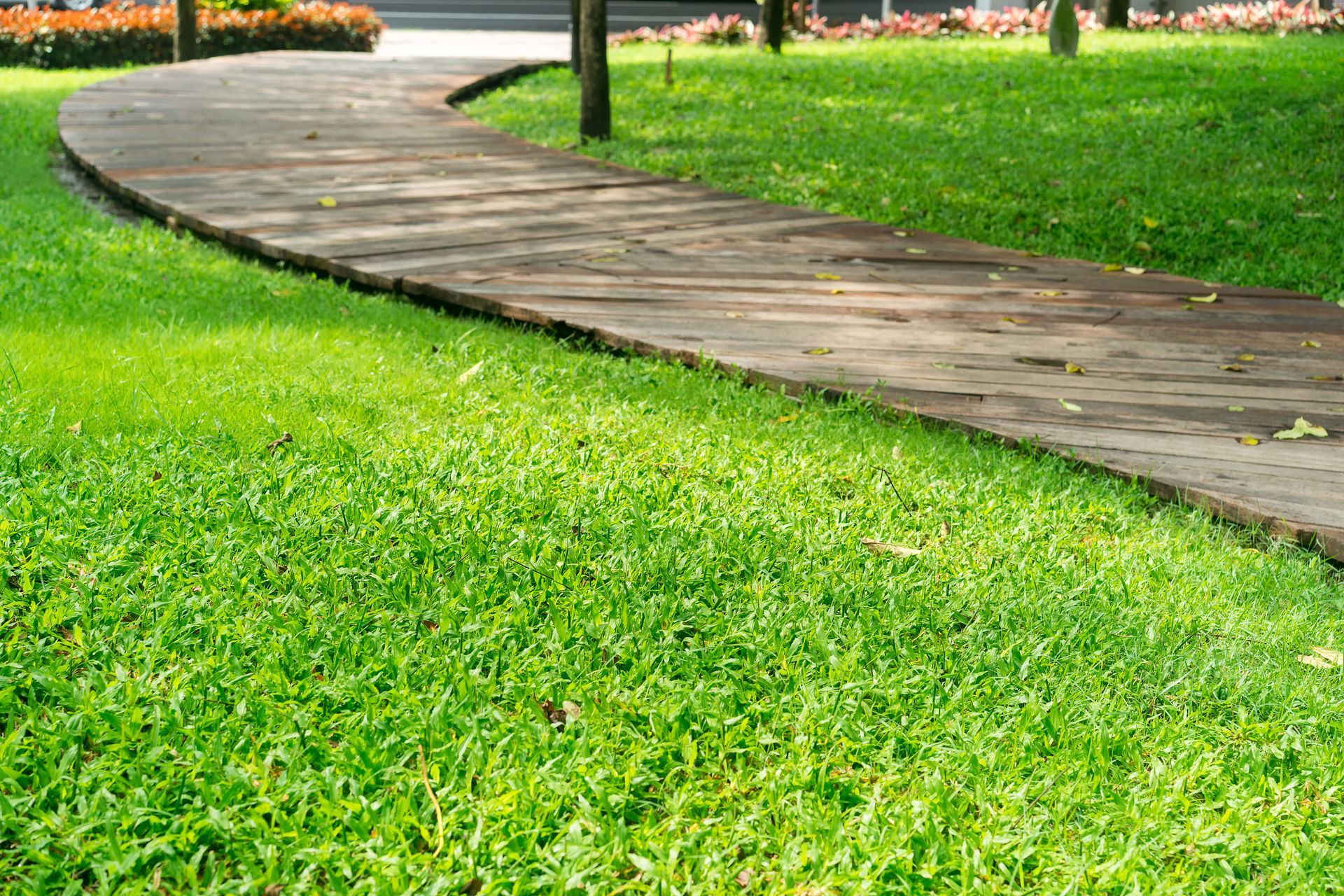 Wooden walkway curves through lush green grass in a park setting.