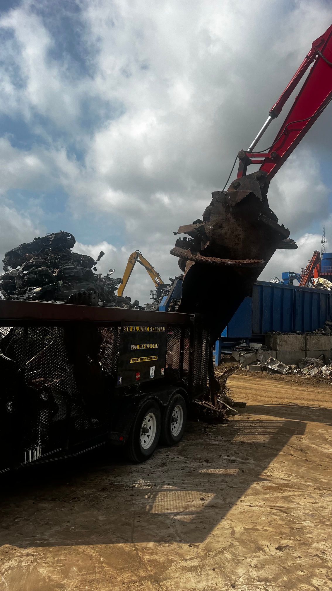 Excavator dumping soil into a dump truck at a construction site under cloudy skies