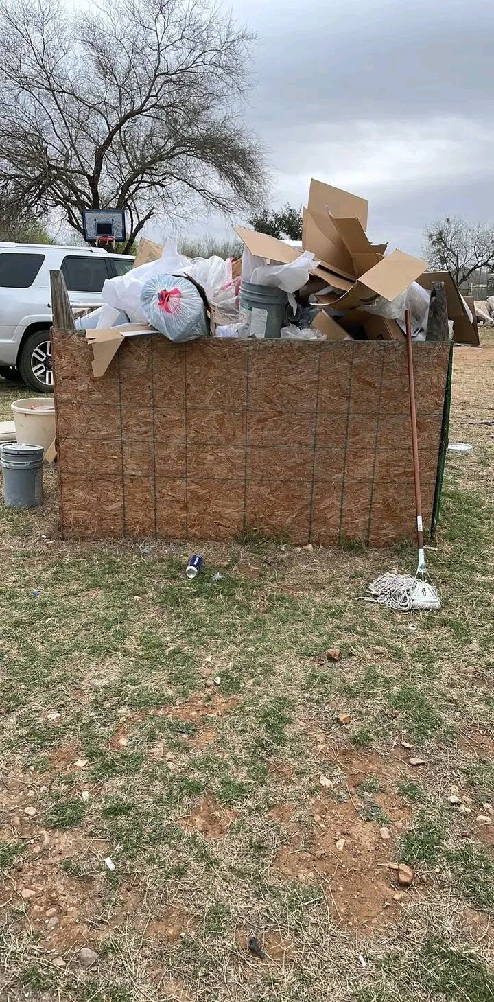 Overfilled outdoor dumpster with trash bags and cardboard beside a white truck in a yard