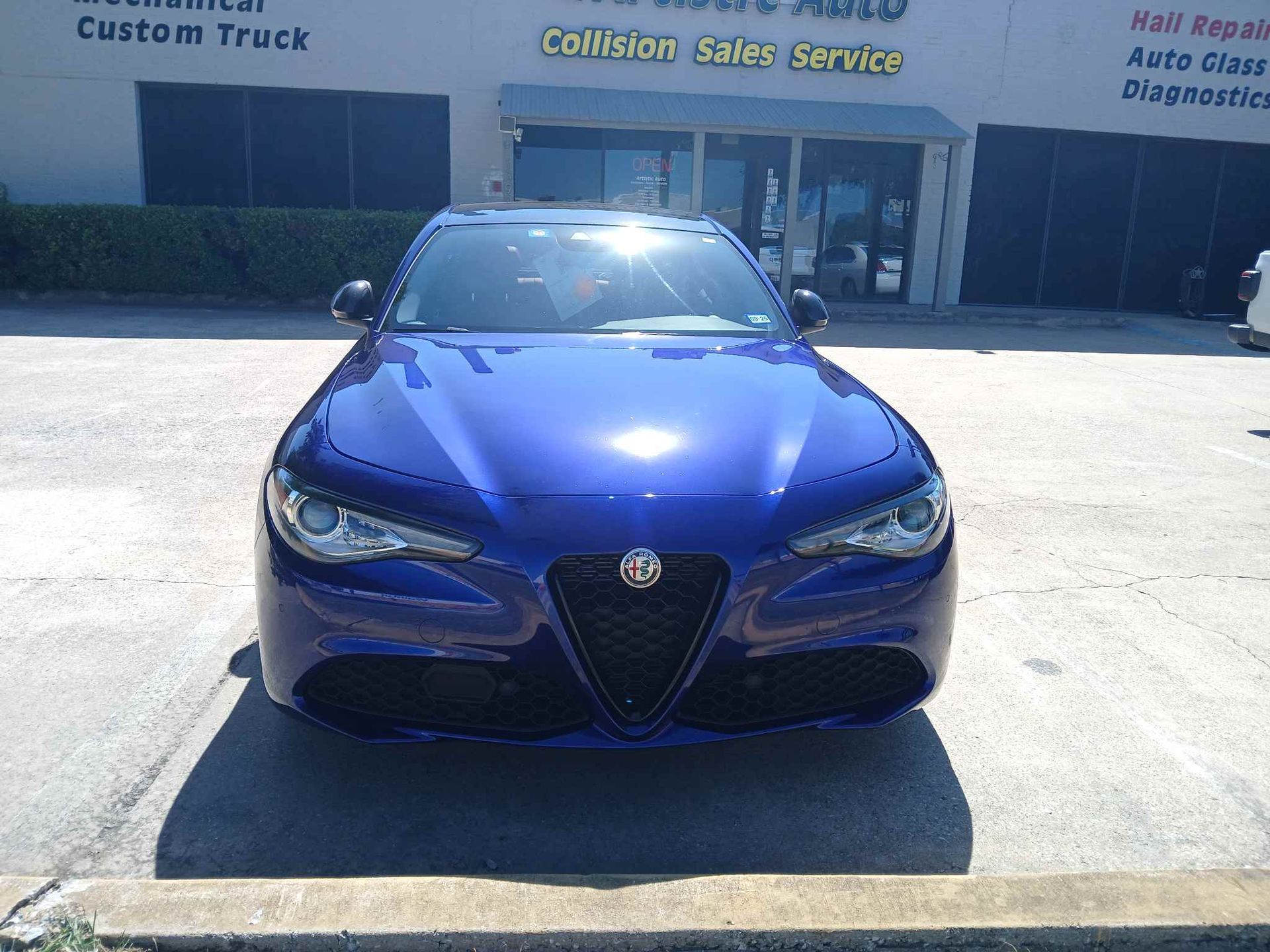 Blue Alfa Romeo sedan parked outside a auto service shop