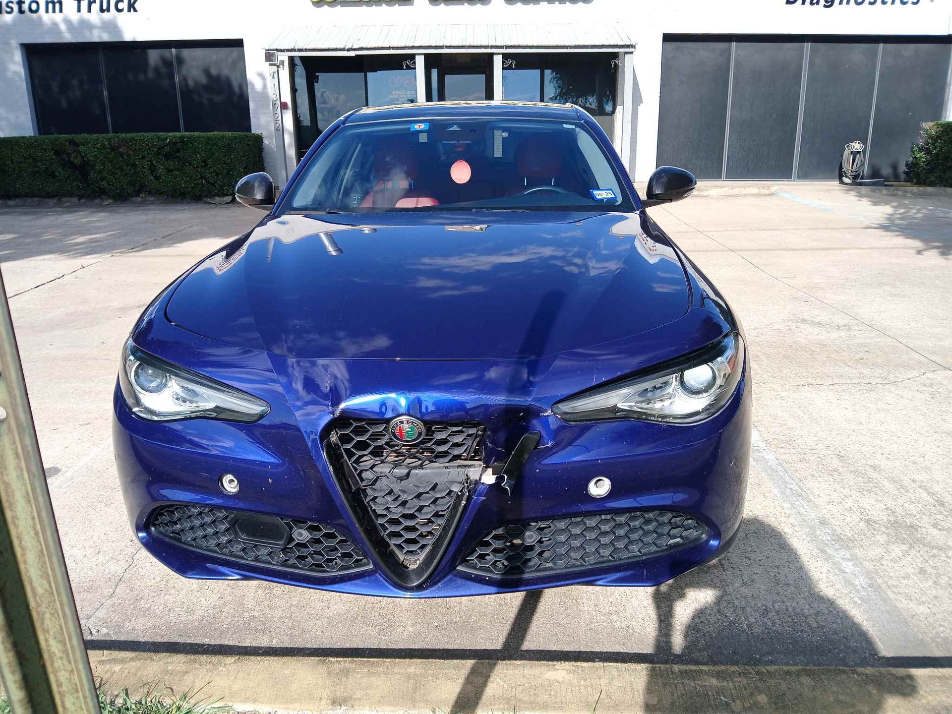 Blue Alfa Romeo sedan parked outdoors in bright sunlight, front view.