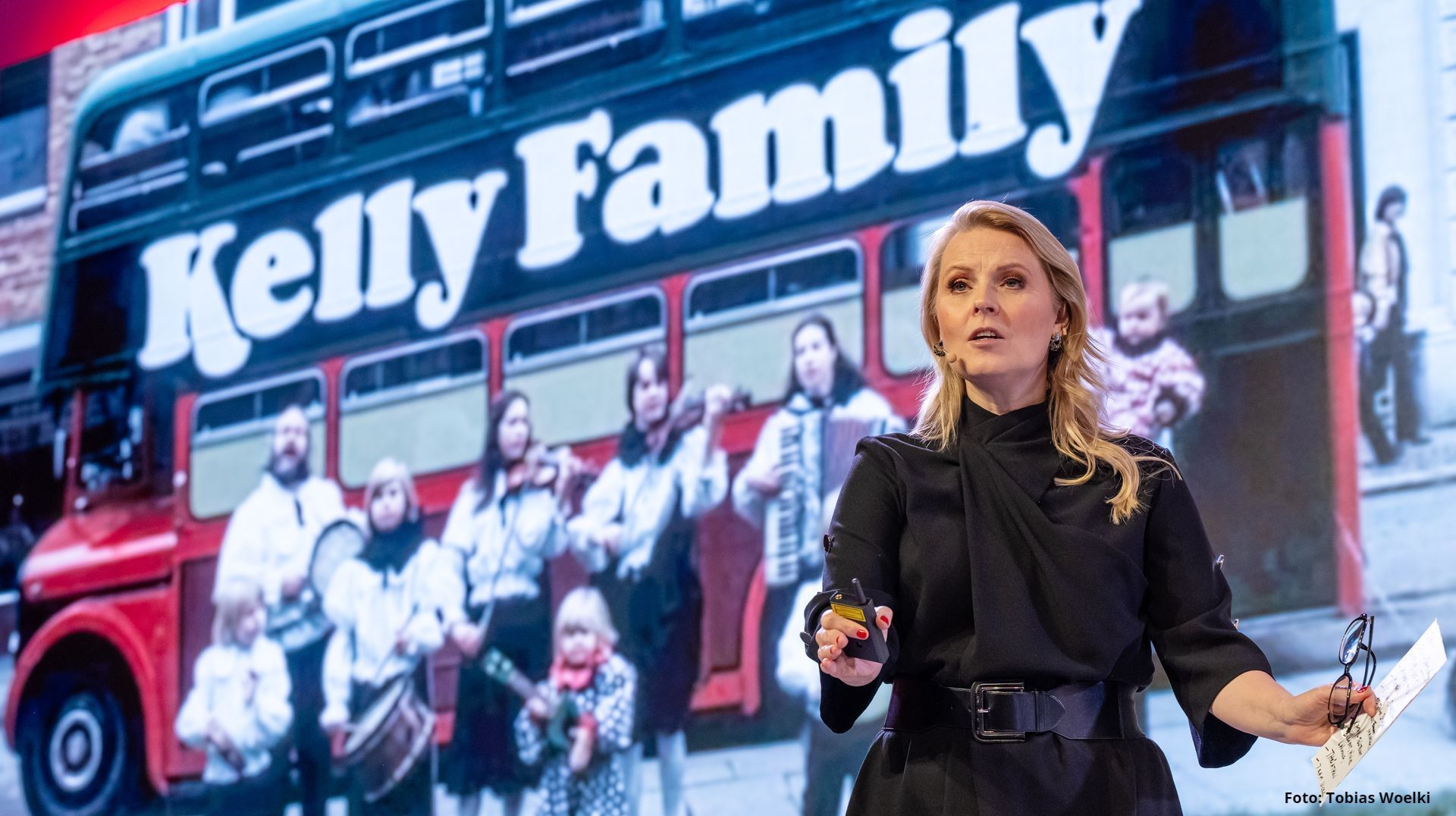 Eine Frau hält vor einem Bus der Kelly Family einen Vortrag.