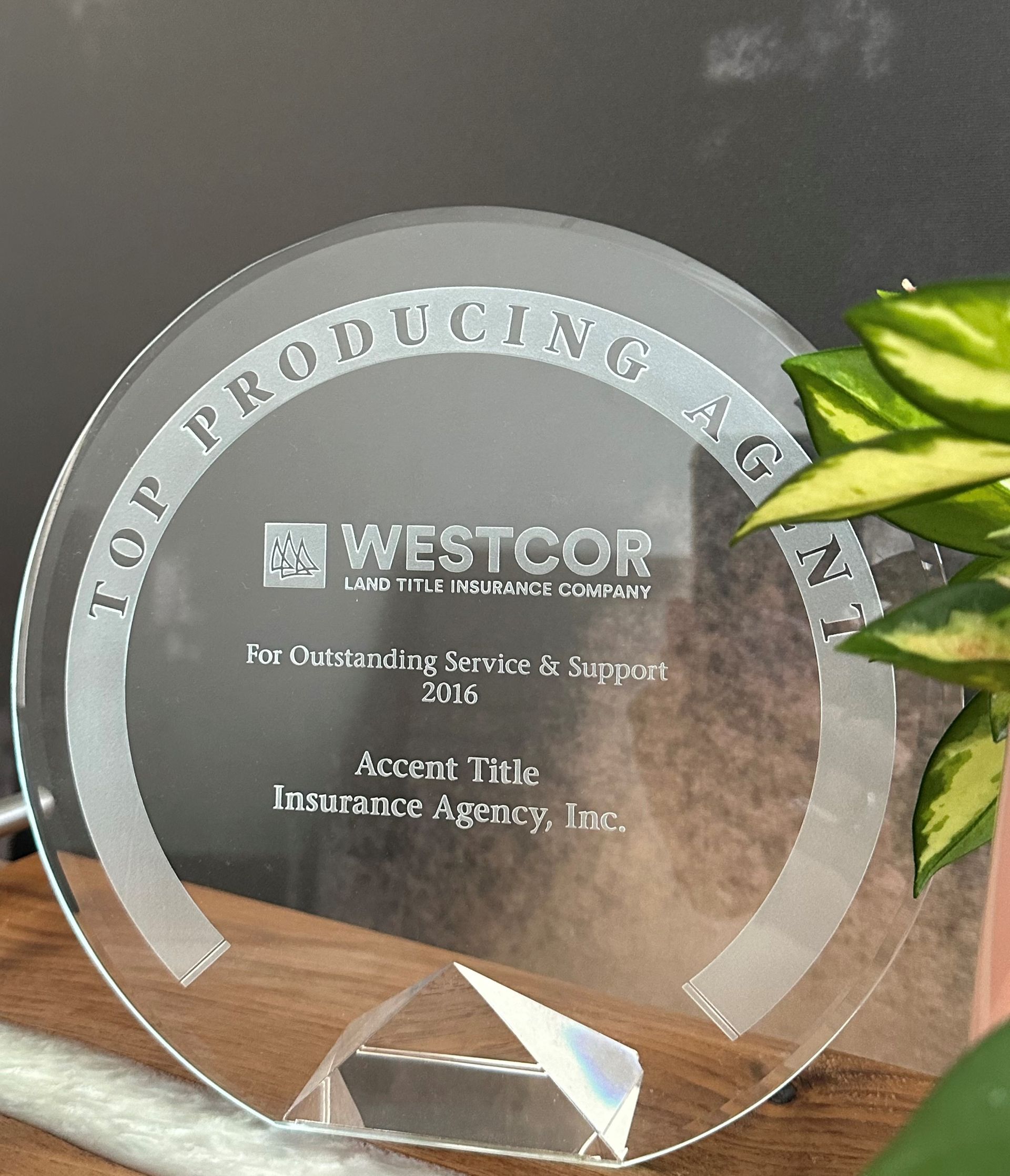A glass plaque that says top producing ign is sitting on a table next to a plant.