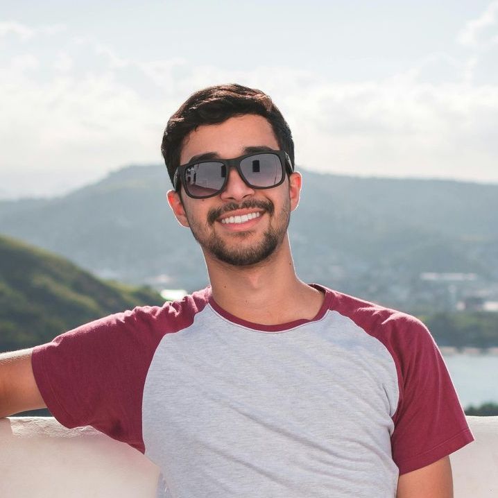 Un homme portant des lunettes de soleil et une chemise marron sourit