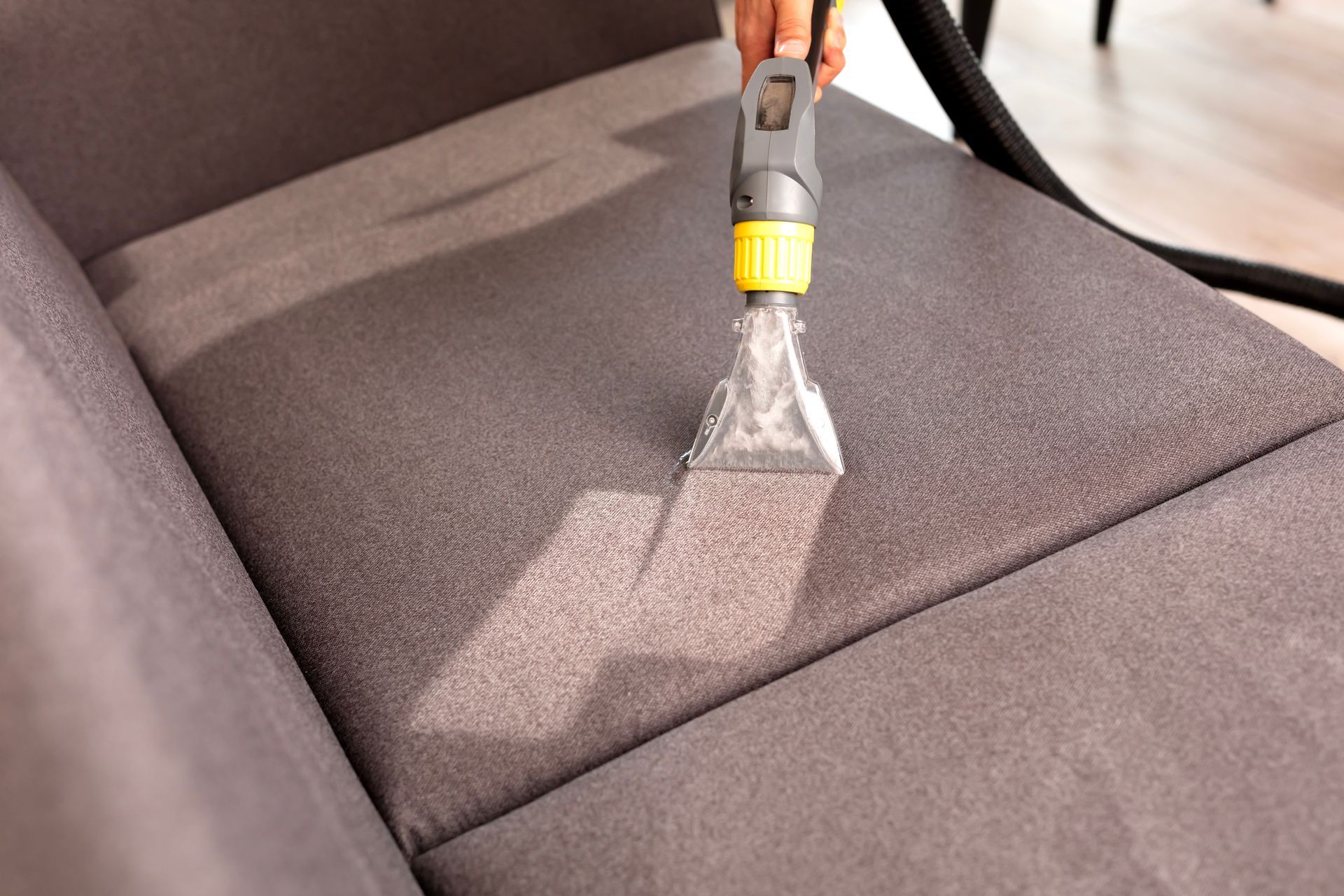 Person using a upholstery cleaner on a gray sofa cushion, removing dirt and stains. Person using a upholstery cleaner on a gray sofa cushion, removing dirt and stains.