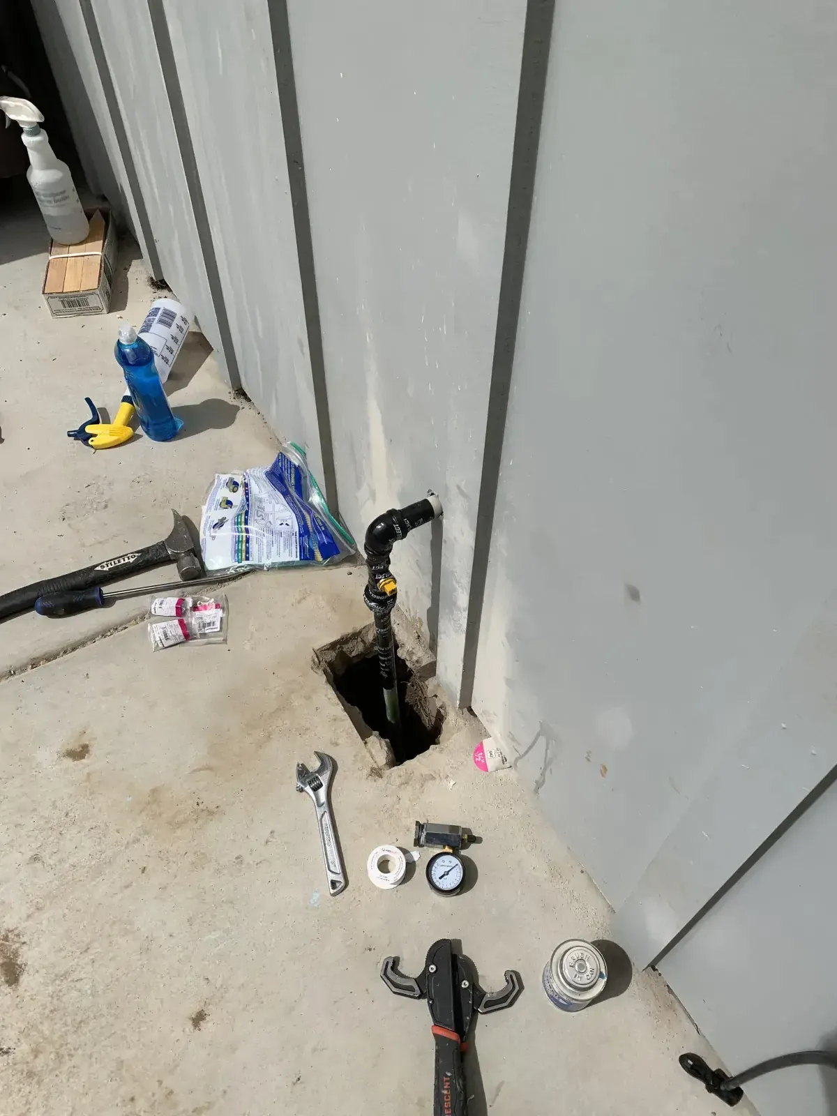 A hose is being installed in a hole in the ground next to a wall.