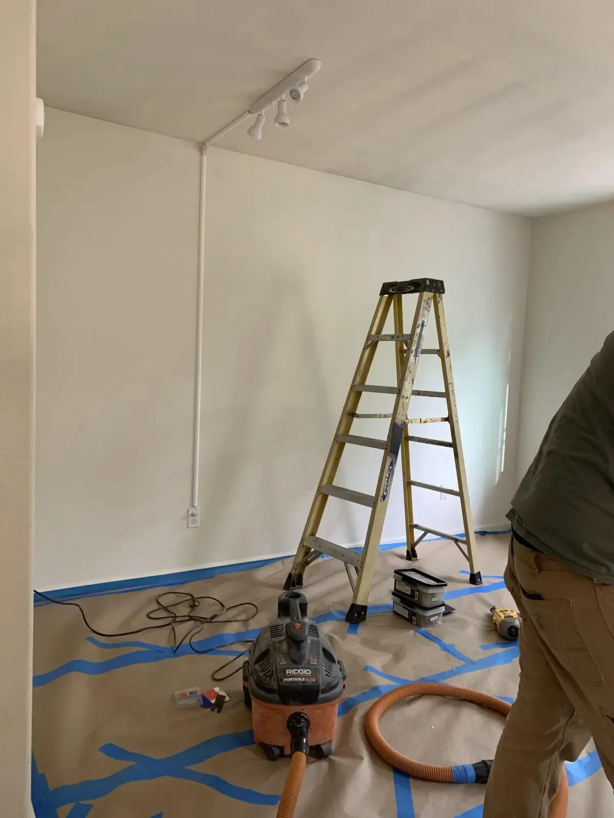 A man is standing in a room with a ladder and a vacuum cleaner.