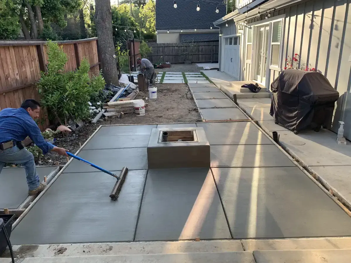 A man is brushing concrete in a backyard with a broom.