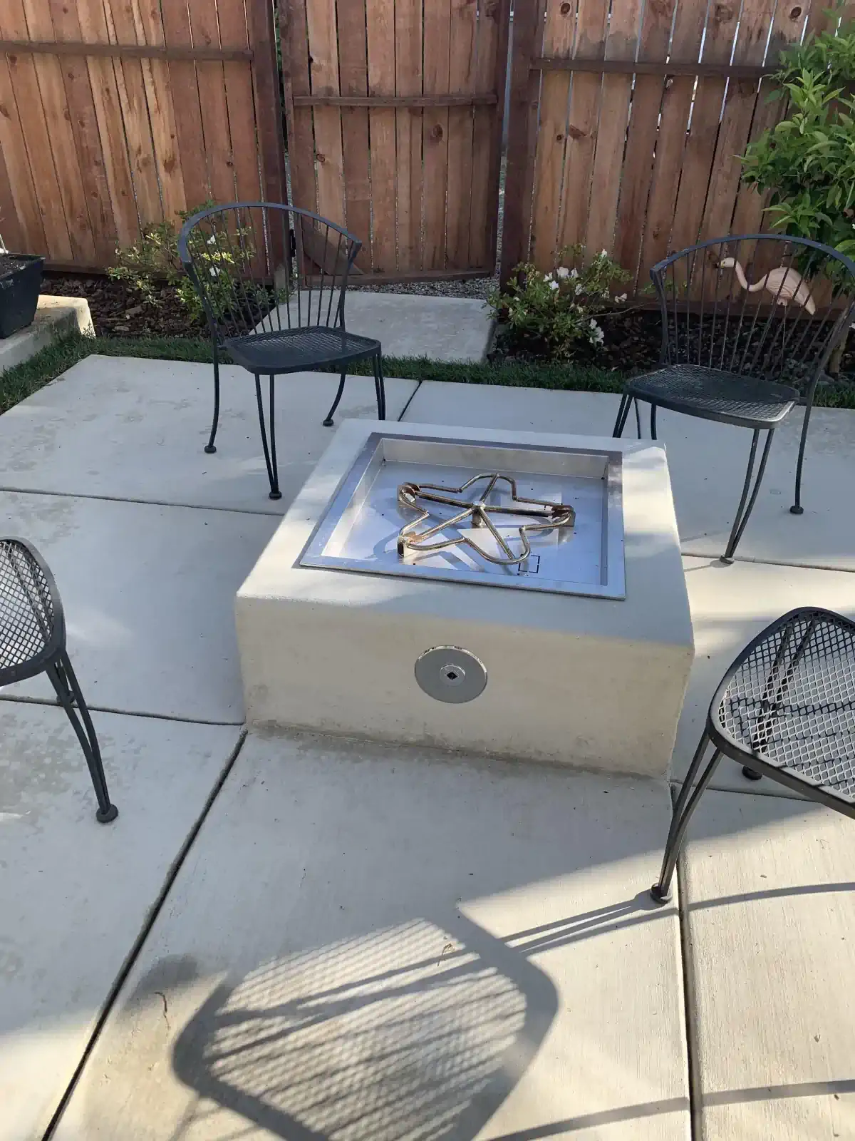 A fire pit on a patio with chairs and a wooden fence in the background.