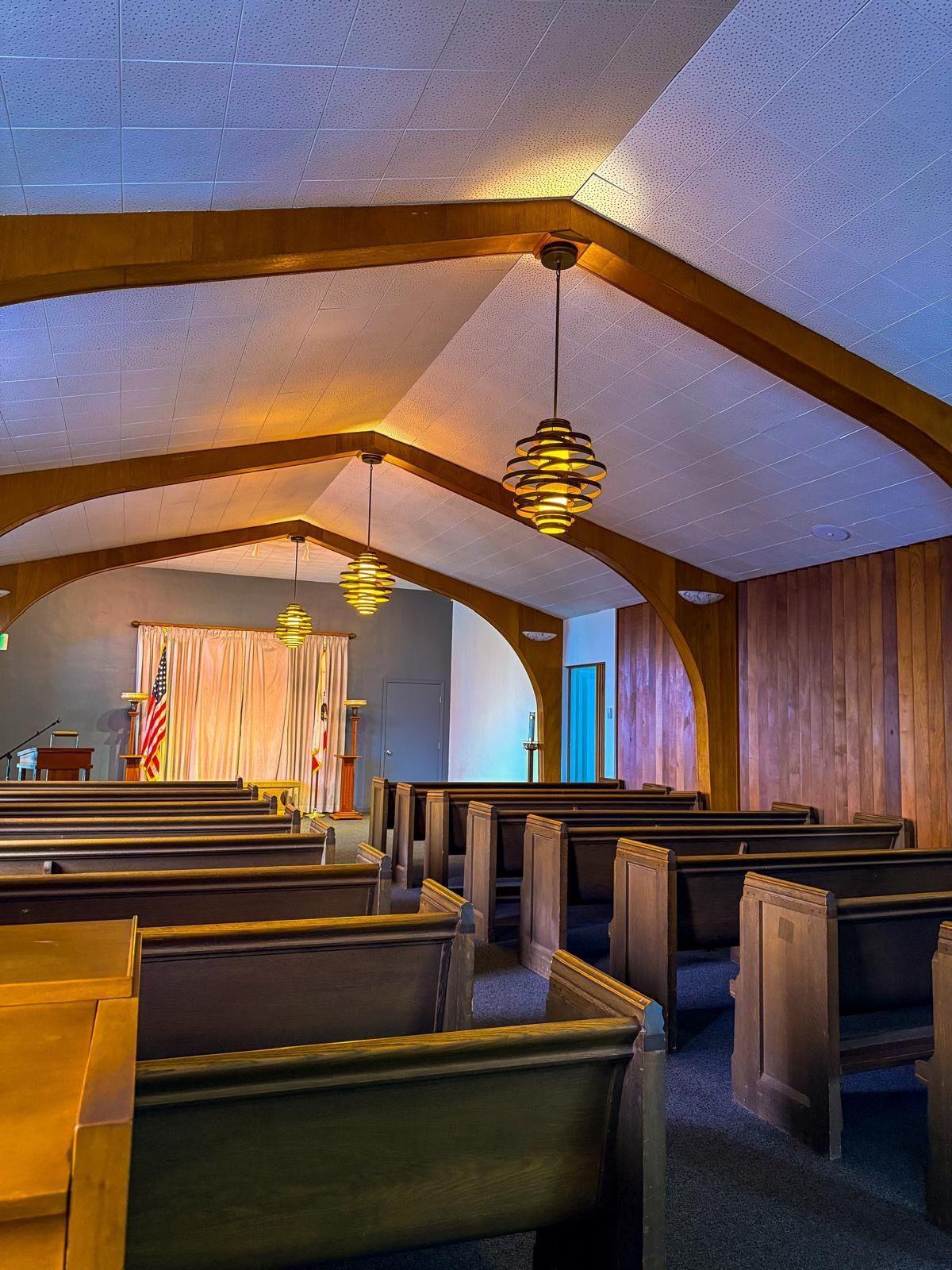 Empty church interior with wooden pews, vaulted ceiling, and hanging lanterns