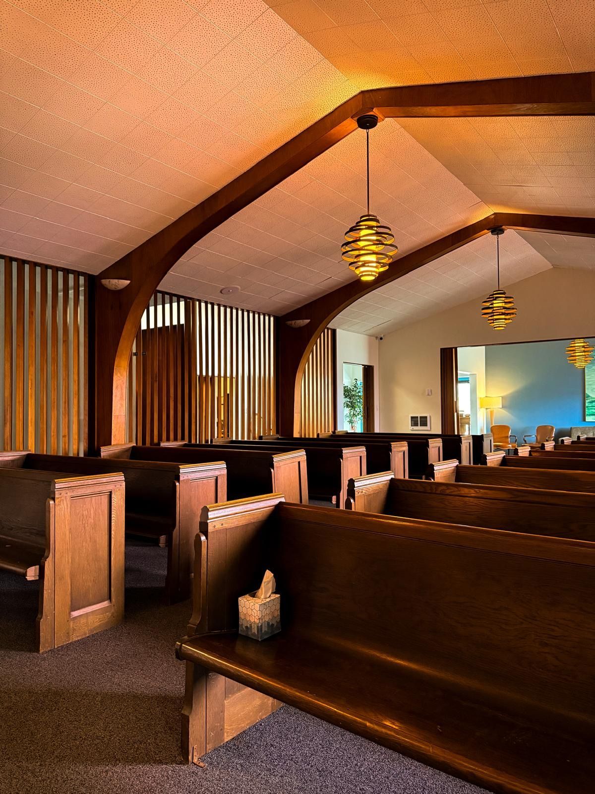 Church interior with wooden pews, vaulted ceiling, and hanging pendant lights