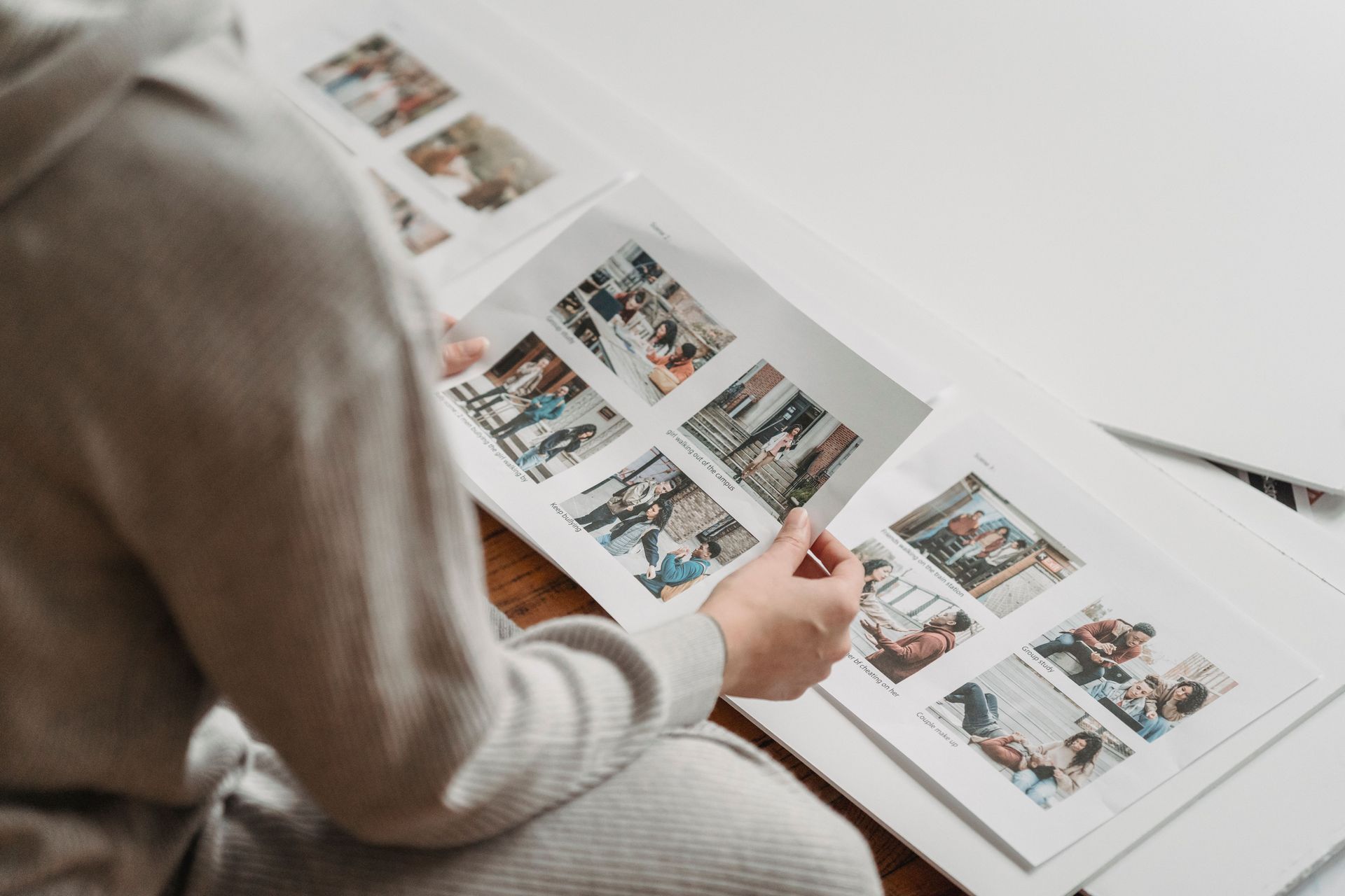 Person reviewing a printed photo album with multiple small images on a white table