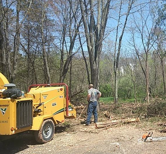 A man is standing next to a tree chipper in the woods.