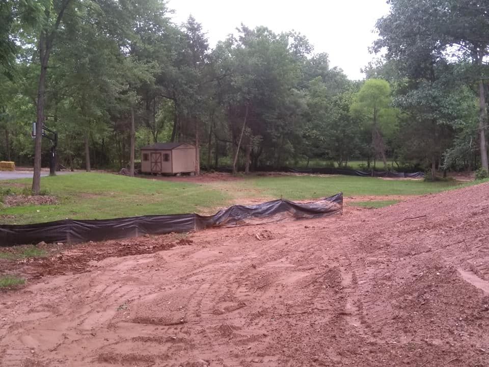 A dirt field with a shed and trees in the background