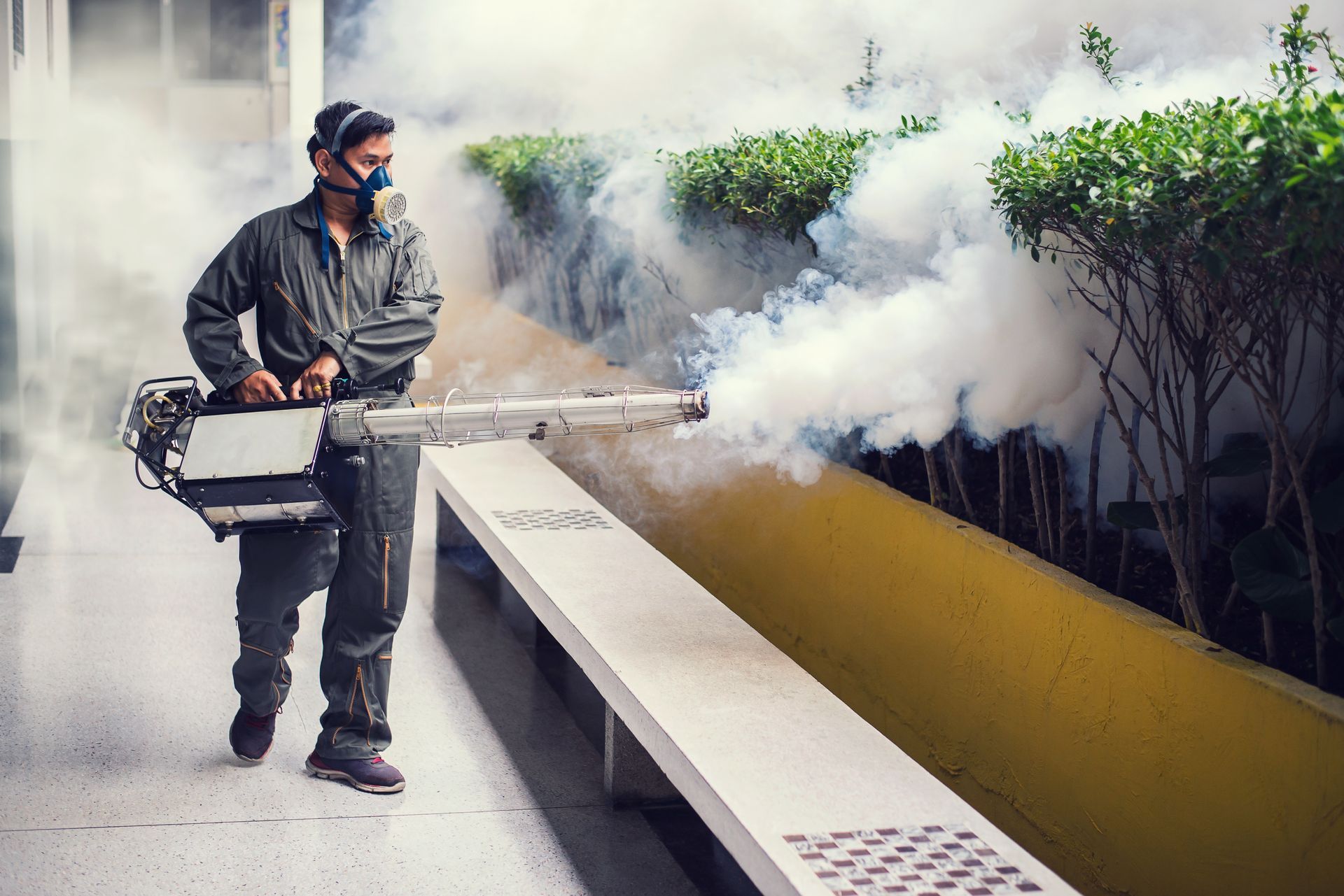 A man wearing a mask is using a machine to spray smoke.